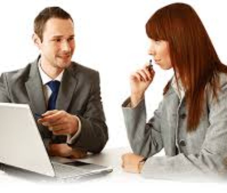 A man and woman sitting at a table with a laptop.