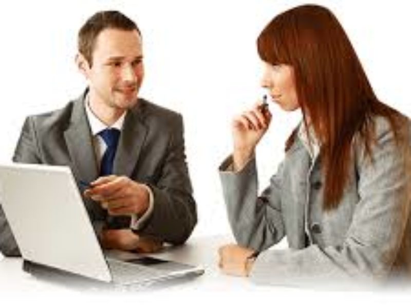 A man and woman sitting at a table with a laptop.