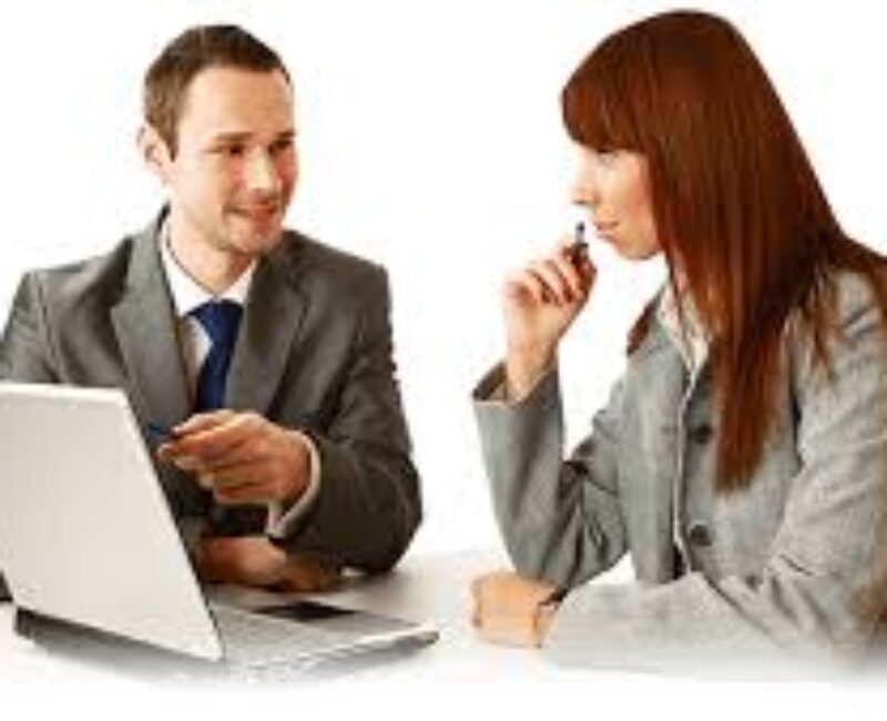 A man and woman sitting at a table with a laptop.