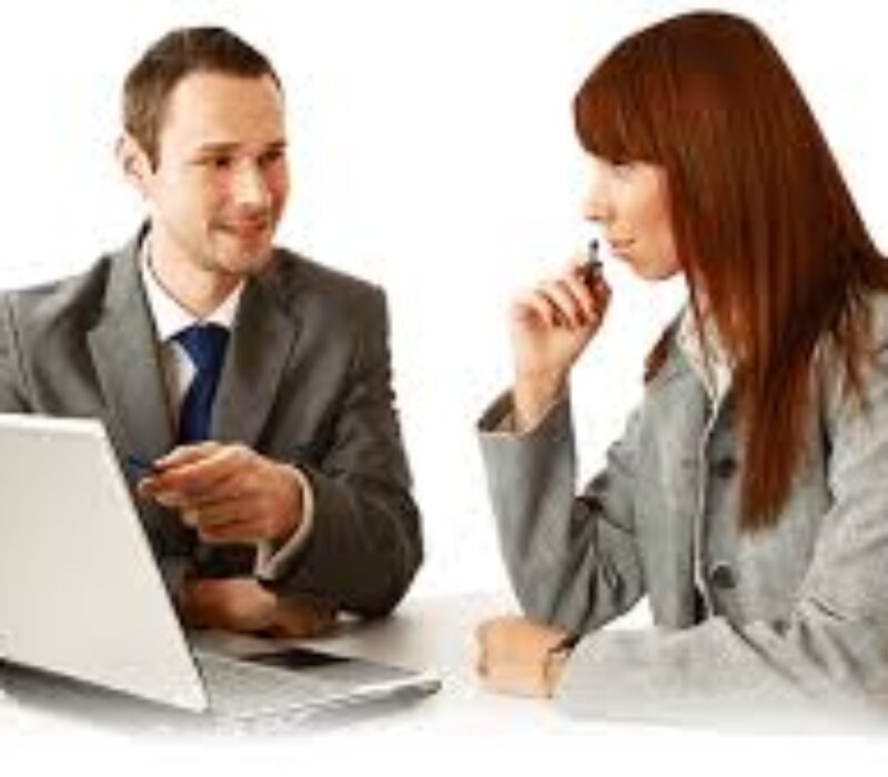 A man and woman sitting at a table with a laptop.