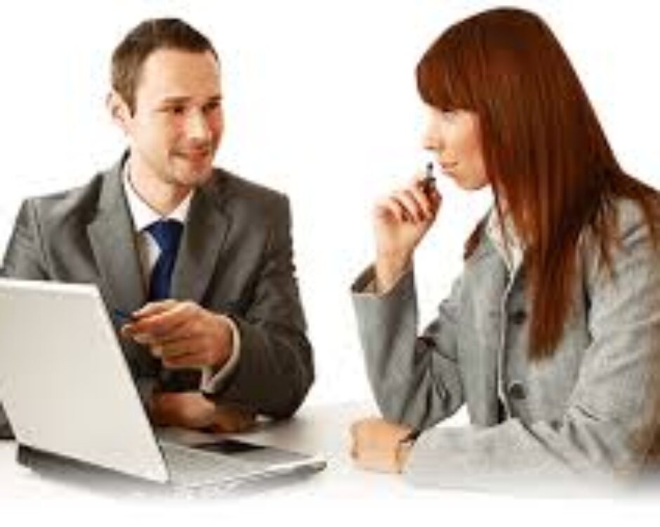 A man and woman sitting at a table with a laptop.