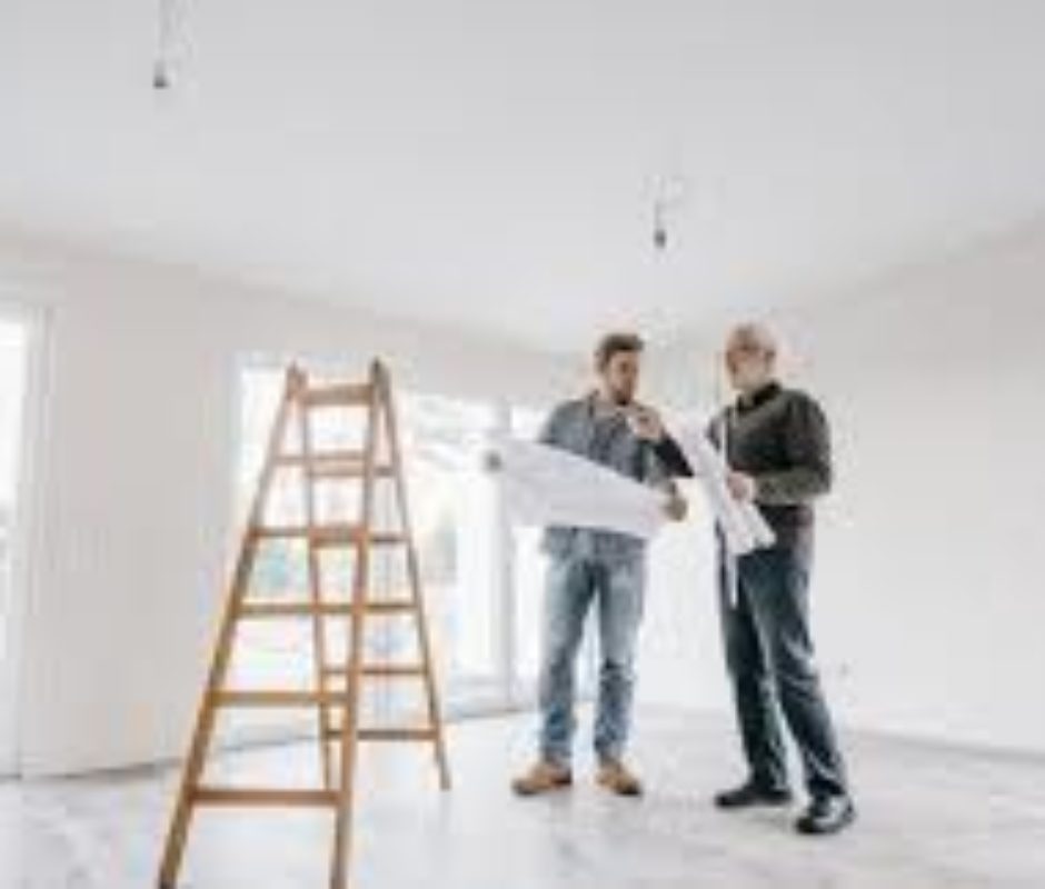 Two men are looking at a plan in the middle of a room.